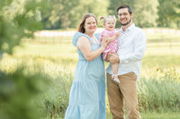 a family of 3 posing near a grassy field at golden hour