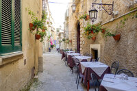 A narrow cobblestone alley lined with tables and chairs covered in white tablecloths evokes a quaint outdoor dining vibe. Vintage lanterns and potted plants adorn the stone walls, reminiscent of the charming streets you'd find on personalized Caribbean getaways.