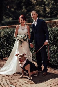 bride and groom standing with dog on leash