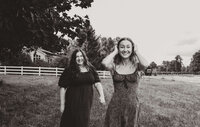 Best friends and event planners in Oregon, Clarae and Taressa, walk in a field towards the camera smiling. 