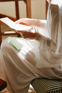 A bride reads a letter from her groom , she is in a gown and is lit by soft window light, it is a tender moment captured by Rebecca Rottcher |Wedding Photographer |Northern Rivers
