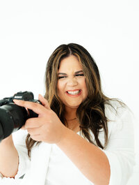 Adriana Montoya Photo smiling, looking at her camera which she is holding out slightly in front of her.