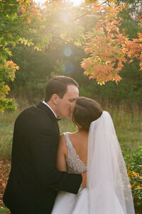 bride and groom  kissing under an orange fall tree in golden hour.