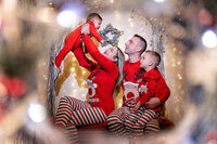 Family wearing red outfits smiling by the Christmas tree in Calini Weddings Studio – joyful festive portrait with warm holiday tones.