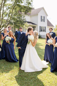 A bride and groom share a kiss as their friends look on and cheer enthusiastically