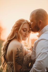 A groom kissing his bride's head at sunset at The Barn on Unity Farm in Princeton, West Virginia