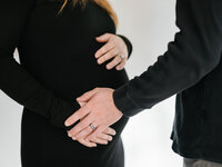 Close-up of two pairs of hands resting over a growing belly, symbolizing love, anticipation, and connection before birth.