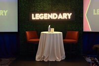 An empty table and chairs on stage with a glowing neon sign behind it that says Legendary