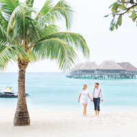 The bride and the groom walking at the Hilton Moorea with the overwater bungalow in the background