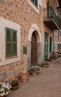 Brick building with green shutters and pots of flowers 