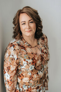 Joanne McCrone smiling in a floral blouse, standing against a neutral background.