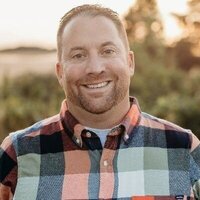 Matt Blaylock, member of Normal 40 smiling in a plaid shirt with farm in background for his testimonial image