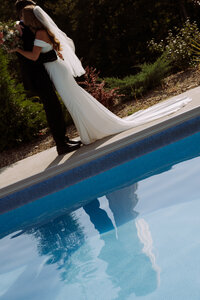 bride and groom standing next to a blue in ground pool