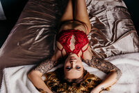 woman looking confident and sexy as she lays on her back in red lingerie on silk sheets and gazes up during her oshkosh boudoir photography session