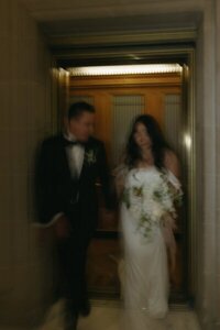 Bride and groom exit elevator hand in hand in San Francisco City Hall by wedding photographer northern california
