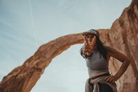 a girl leaning down towards the camera and holding up the peace sign under Jeep Arch in Moab, Utah