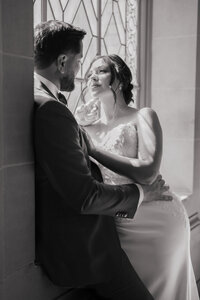 Intimate wedding photography of bride and groom sharing a quiet moment by a window in black and white.
