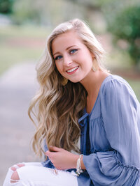 Beautiful high school senior girl with long blonde hair sitting on a pathway wearing a soft blue dress in a Charleston park