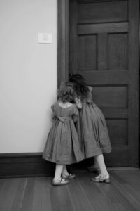two flower girls in dresses peeking into the bridal suite