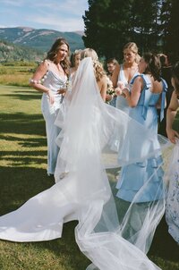 Veil and train of bride's dress trail behind her as she is surrounded by bridesmaids in at Camp Hale in Vail, Colorado.