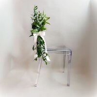Bundle of greenery tied with a ribbon on a clear chair