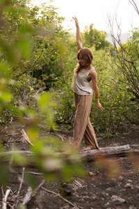yoga teacher walking on a log with green trees behind her
