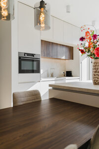 jongedame in keuken met koffiekop in haar handen, blond, bril, beige shirt met witte jeans, lacht