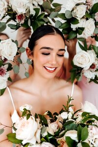 Bride with bold eyebrows surrounded by floral bouquets in white gown