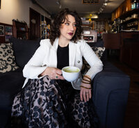 Woman in a white blazer sitting on a couch with a cup of tea in her hand