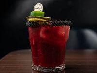 red colored drifter's cocktail with lime and jalapeno garnish in a cocktail glass rimmed with black salt