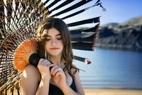 High school senior at a lake holding a large tattered paper umbrella.