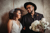 A smiling couple shares a joyous moment, the bride in a white sequined dress and the groom in a black suit with a floral boutonniere