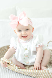 Baby sitting in a basket with a pink bow on its head for photography session in a studio in Dothan Alabama