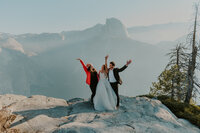 bride, groom and woman at the top of a mountain hands in the air