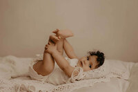 a baby girl laying on her back wearing all white grabbing her feet in a beautiful studio in Rochester, NY