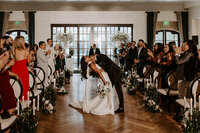 A groom leans a bride over for a kiss while everyone cheers on their wedding day at The Stirling Club in Las Vegas.