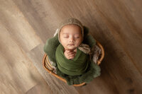 Studio newborn wrapped in green with rabbit fur in a bamboo basket