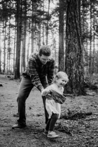 black and white photograph of a dad and his daughter laughing and running in the woods