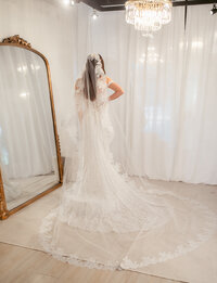 Bride in boutique on the stage in mirror with wedding dress and long veil. Trying on dresses at our boutique.