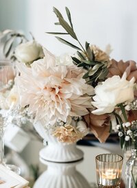 Op tafel staat een vaas met romantische bloemen. dahlia cafe aut lait, olijftak, rozen, anjers