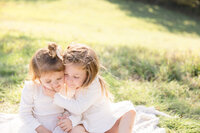 Twin toddler girls cuddling with their faces in white dresses at Phillips Park in Beavercreek, Ohio.