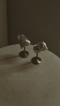 Two seashells mounted on small metal stands are used as candle holders. They are placed on a round concrete table with a dark background.