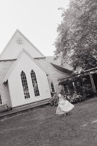 Bride twirling in front of a white chapel after her ceremony — black and white wedding portrait captured in Alabama by EC Photography
