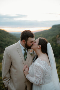 elopement photo of bride and groom kissing on an overlook at sunset