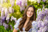 charlotte catholic senior sits surrounded by wisteria wearing a blue and purple toned dress