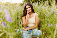 pretty teen girl looking super confident as she sits in a flower field and rests her chin against her fingers captured by Ashley Kalbus