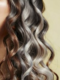 A detailed close-up of healthy, wavy hair, showcasing a beautiful blend of dark and light, possibly gray or blonde, highlights with defined curls.