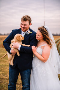 bride and groom look at new puppy and smile
