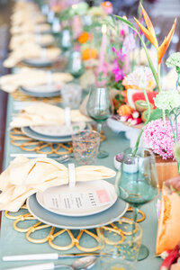 Whimsical wedding table with lavender florals, green goblets, woven chargers, and colorful menus, styled by Eventive Designs for a bold celebration.