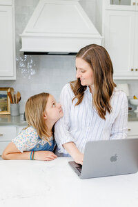 Jessie working at her laptop while smiling at her daughter